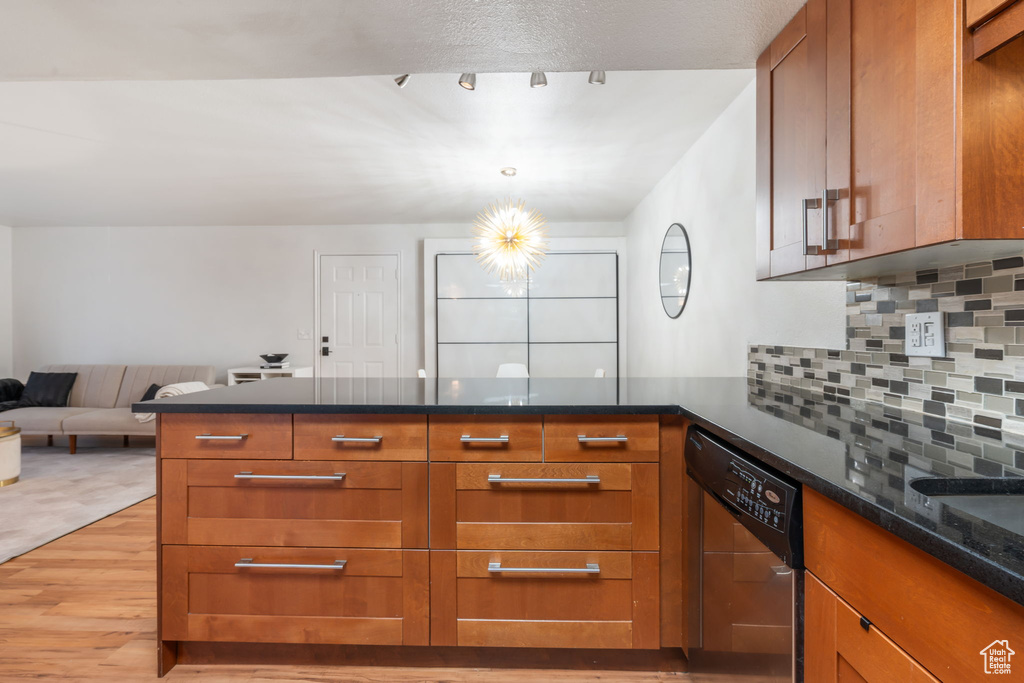 Kitchen featuring pendant lighting, stainless steel dishwasher, light hardwood / wood-style floors, dark stone counters, and backsplash