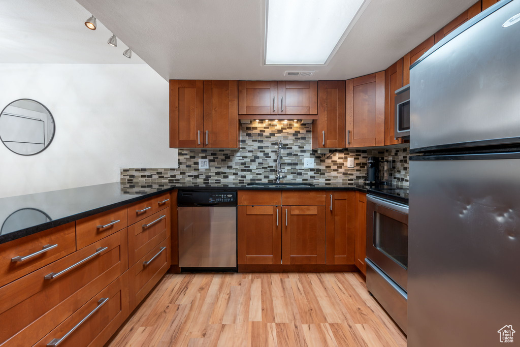 Kitchen with tasteful backsplash, appliances with stainless steel finishes, light hardwood / wood-style flooring, and sink
