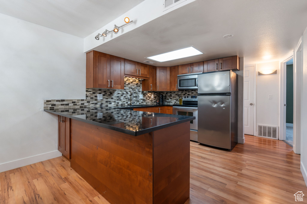 Kitchen with tasteful backsplash, light wood-type flooring, a skylight, appliances with stainless steel finishes, and kitchen peninsula