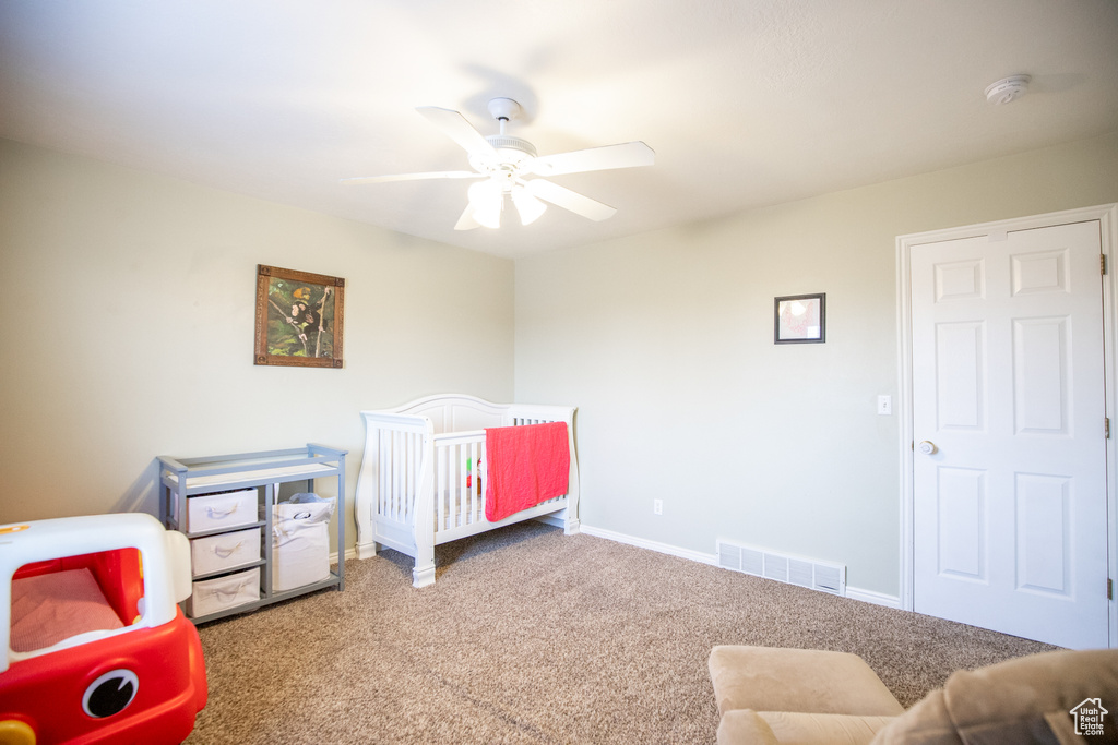 Bedroom featuring a nursery area, ceiling fan, and light colored carpet