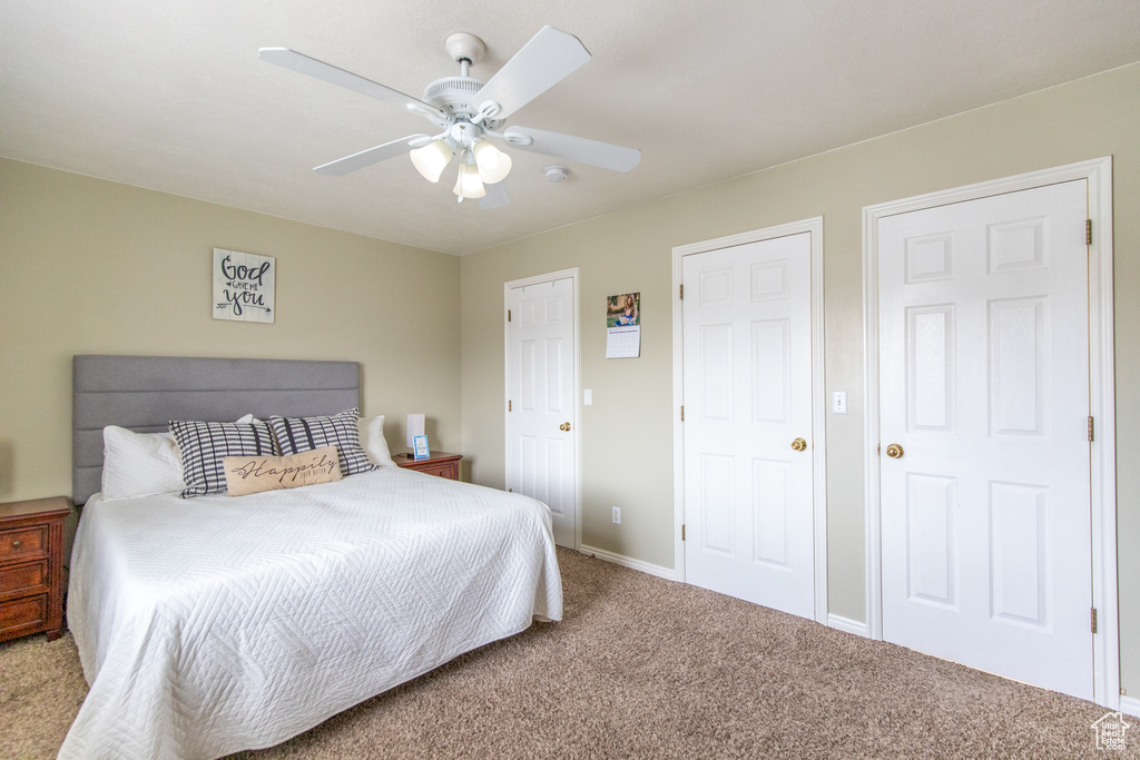 Bedroom featuring light colored carpet, two closets, and ceiling fan