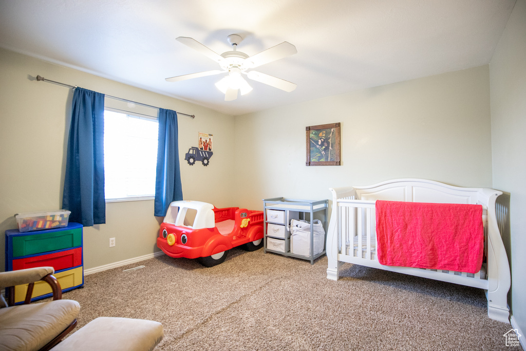 Bedroom featuring dark colored carpet, a nursery area, and ceiling fan