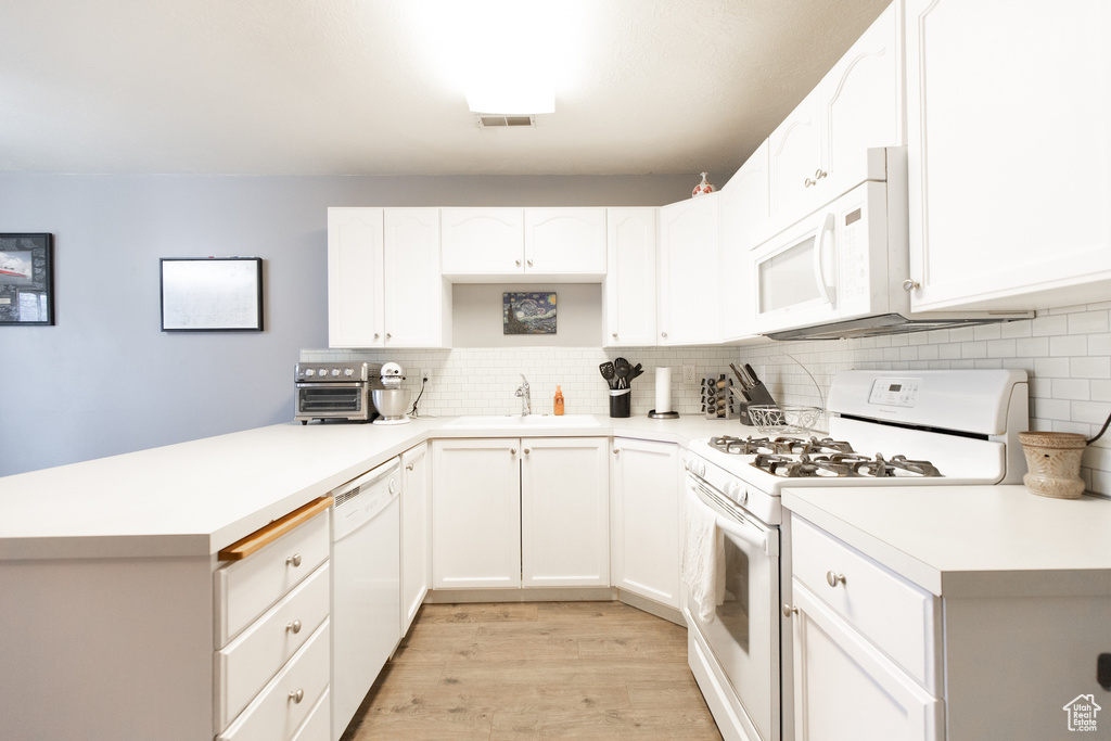 Kitchen with tasteful backsplash, white appliances, white cabinetry, and light hardwood / wood-style flooring