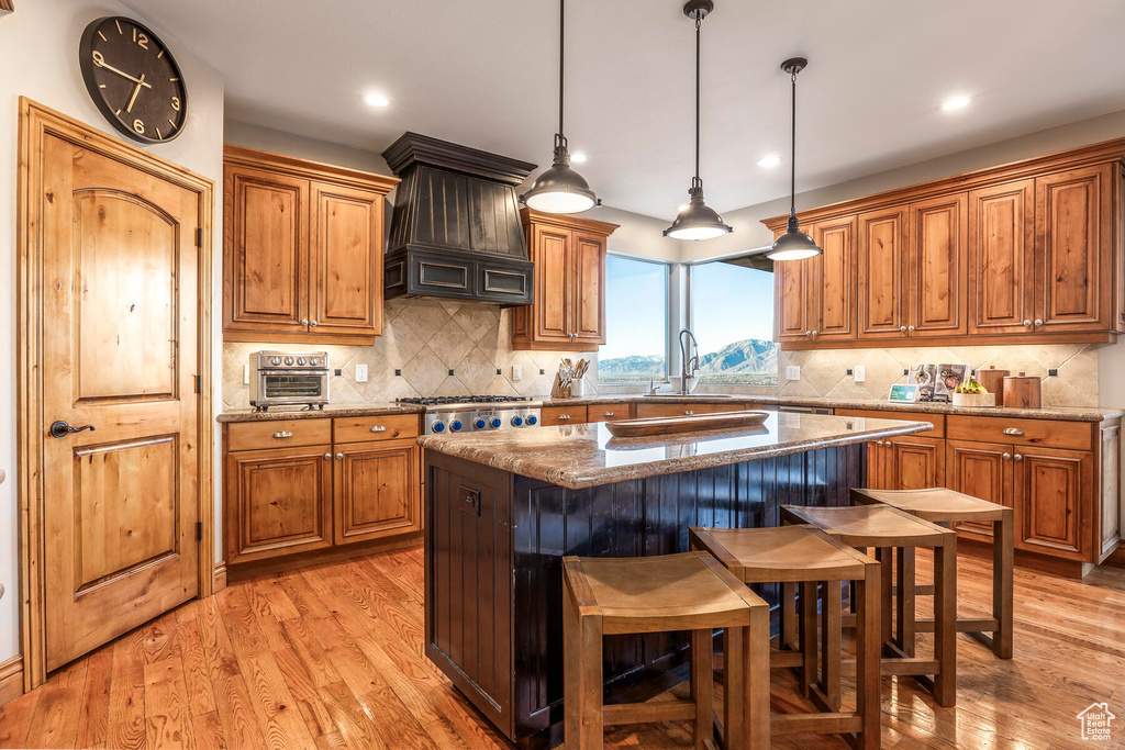 Kitchen featuring sink, stone counters, custom exhaust hood, a center island, and light hardwood / wood-style floors