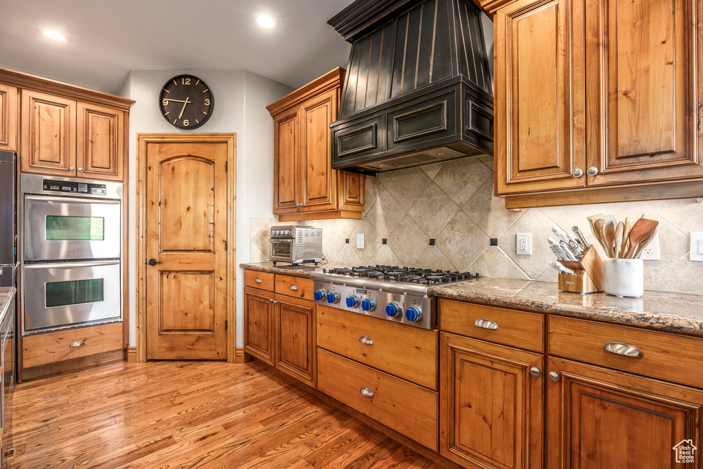 Kitchen featuring tasteful backsplash, stone countertops, light wood-type flooring, and appliances with stainless steel finishes