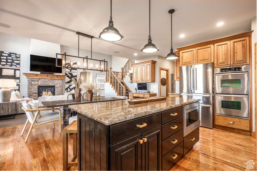 Kitchen with a fireplace, hanging light fixtures, appliances with stainless steel finishes, and light hardwood / wood-style flooring