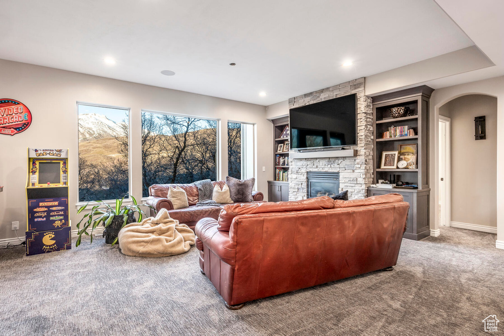 Living room with a stone fireplace, carpet flooring, and built in shelves