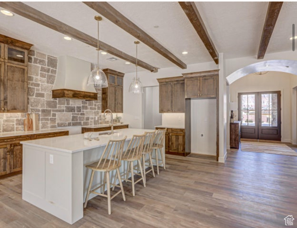 Kitchen featuring french doors, a center island with sink, custom exhaust hood, and light hardwood / wood-style floors