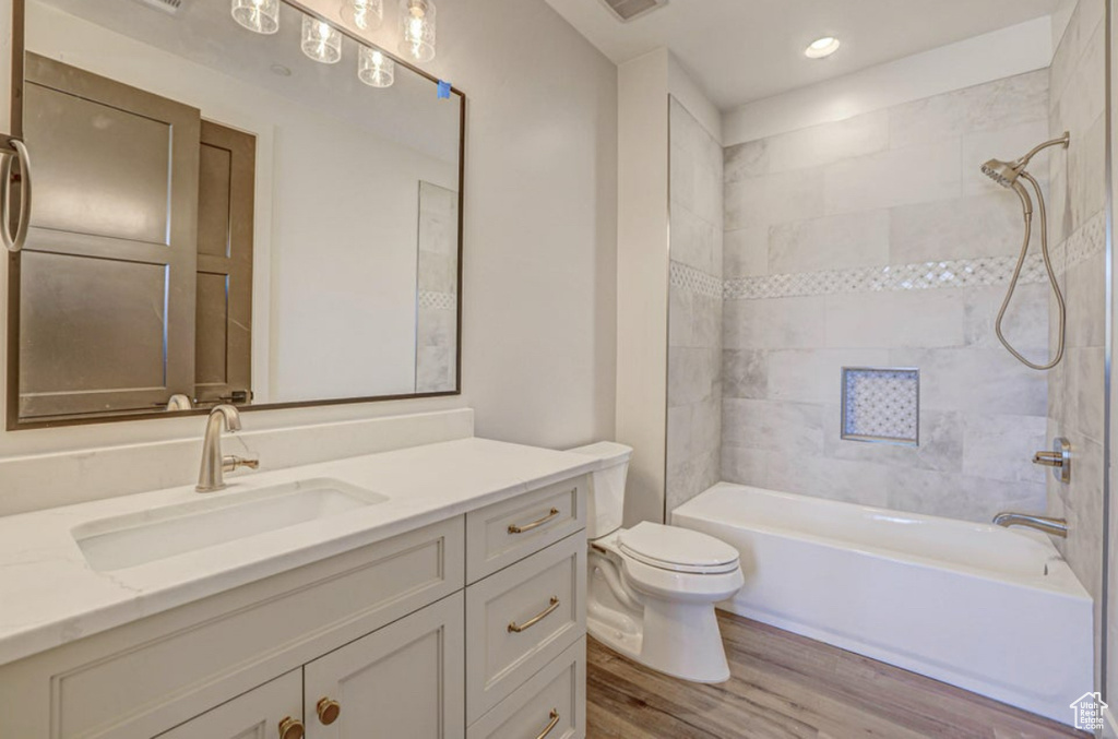 Full bathroom featuring hardwood / wood-style floors, large vanity, toilet, and tiled shower / bath
