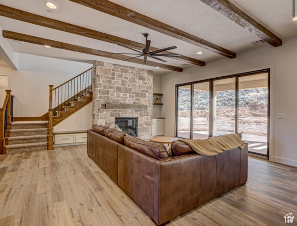 Living room featuring a fireplace, ceiling fan, beam ceiling, and light hardwood / wood-style flooring