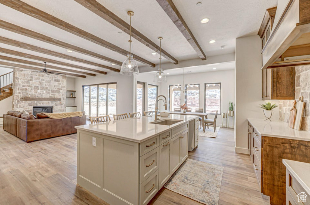 Kitchen featuring a center island with sink, decorative light fixtures, a fireplace, sink, and light hardwood / wood-style flooring