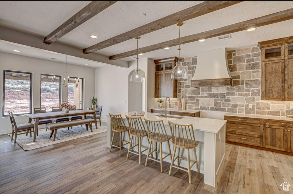 Kitchen with a kitchen island with sink, light hardwood / wood-style flooring, sink, hanging light fixtures, and a kitchen bar