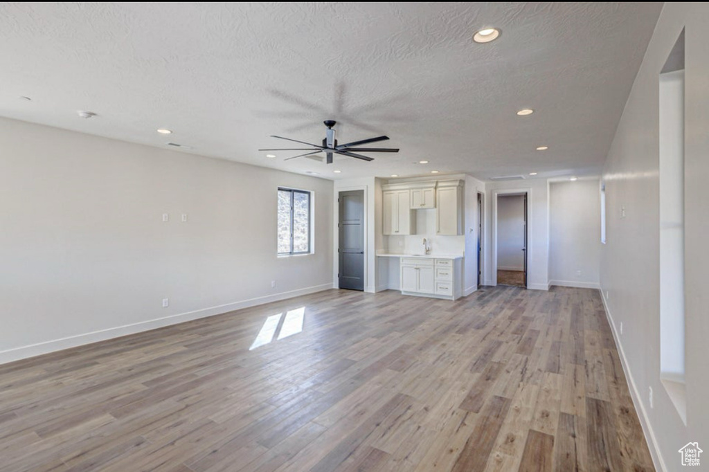 Unfurnished living room with sink, a textured ceiling, light hardwood / wood-style floors, and ceiling fan