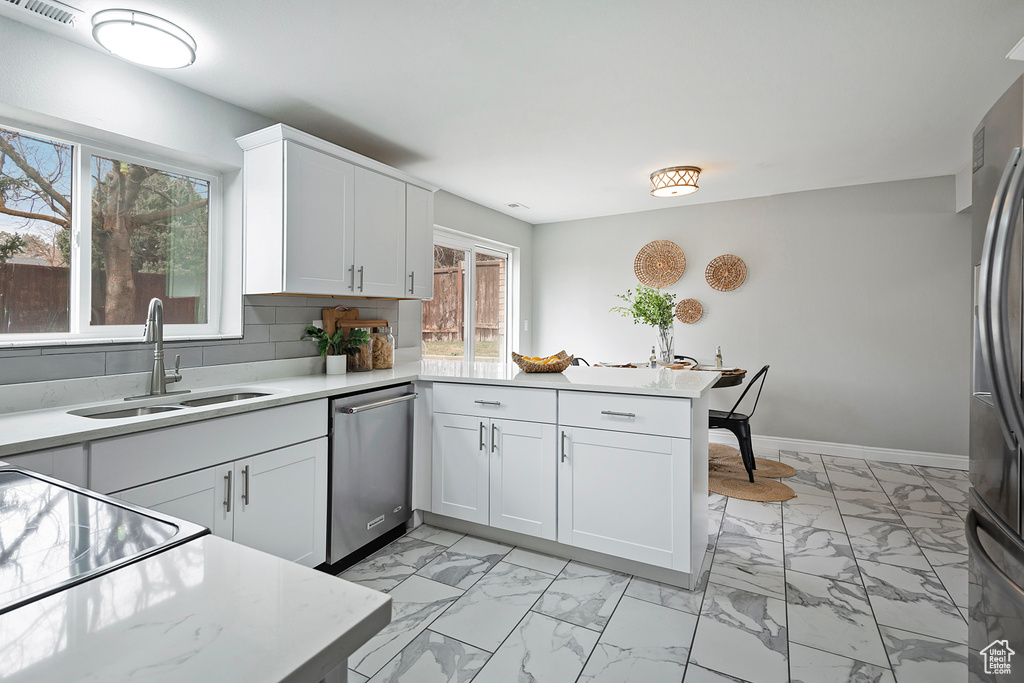Kitchen with kitchen peninsula, stainless steel appliances, light tile floors, tasteful backsplash, and white cabinetry