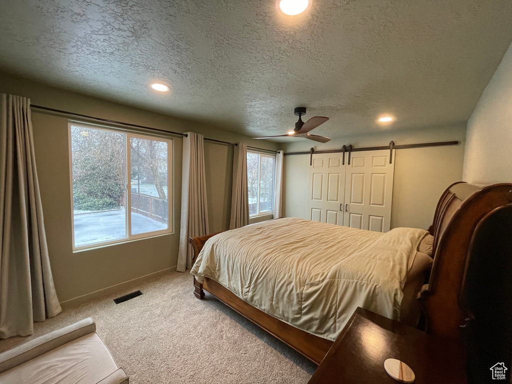 Carpeted bedroom with a textured ceiling, a barn door, and ceiling fan
