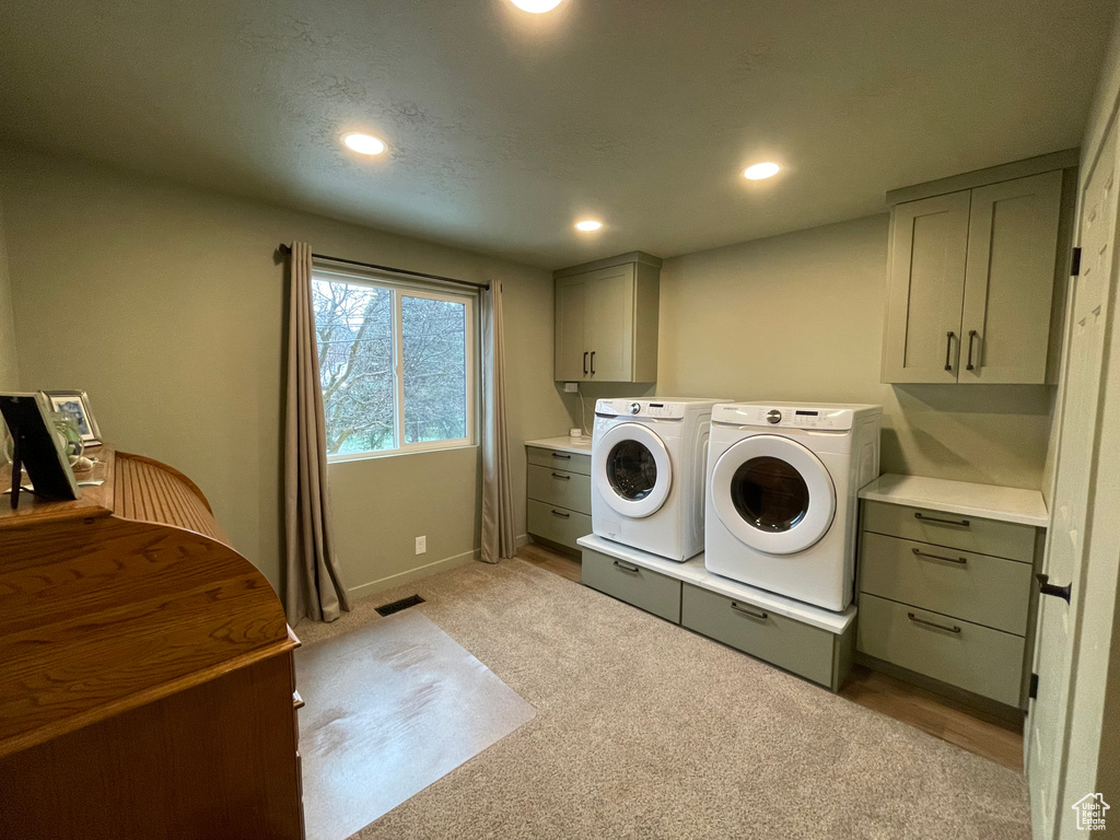 Clothes washing area with cabinets, light carpet, and washing machine and dryer