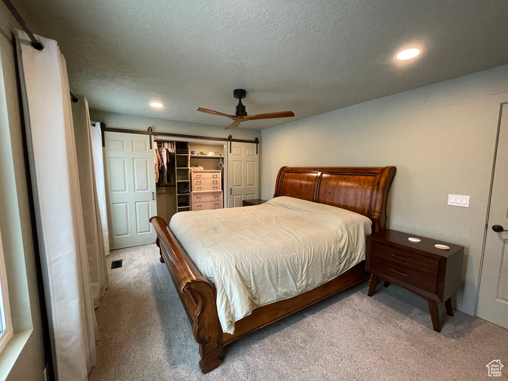 Carpeted bedroom with ceiling fan, a barn door, a textured ceiling, a closet, and a walk in closet