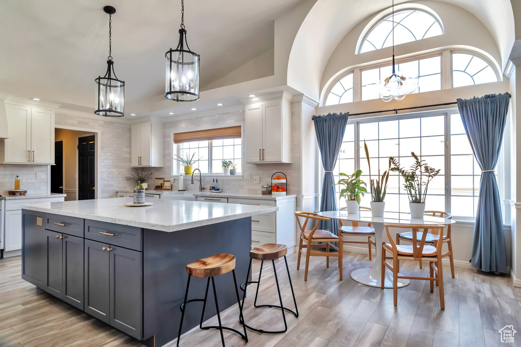 Kitchen featuring backsplash, white cabinets, light stone countertops, and a center island
