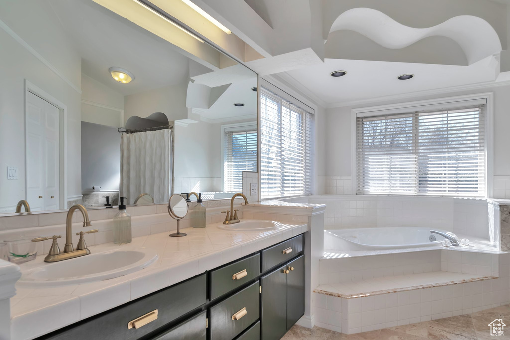 Bathroom with plenty of natural light, dual bowl vanity, tile flooring, and tiled bath