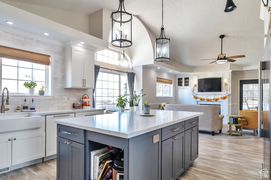 Kitchen featuring ceiling fan with notable chandelier, hanging light fixtures, light hardwood / wood-style floors, a center island, and white cabinetry
