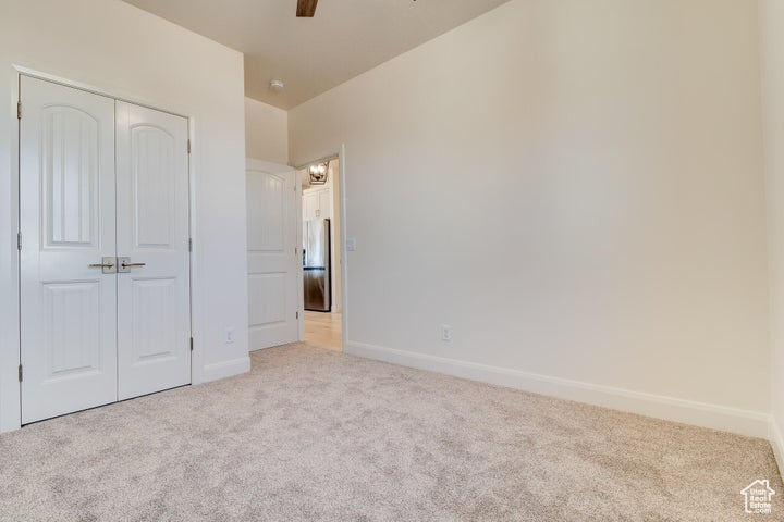 Unfurnished bedroom with stainless steel refrigerator, light colored carpet, ceiling fan, and a closet