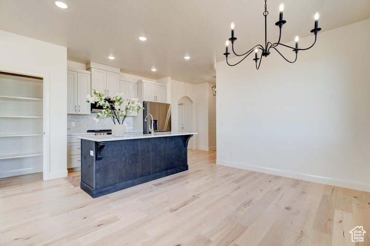 Kitchen featuring light hardwood / wood-style floors, a kitchen island with sink, white cabinets, and backsplash