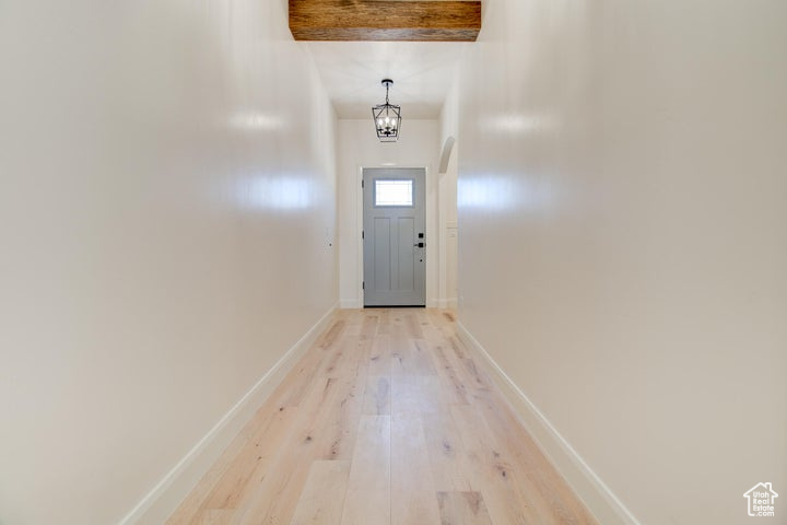 Doorway to outside with beam ceiling and light wood-type flooring