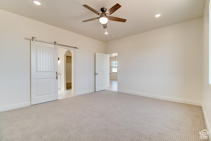 Unfurnished bedroom with a barn door, ceiling fan, and light colored carpet