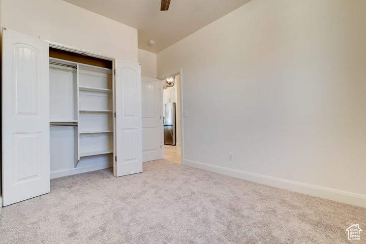 Unfurnished bedroom featuring a closet, light carpet, and ceiling fan
