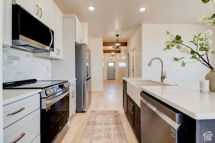 Kitchen with white cabinets, pendant lighting, tasteful backsplash, appliances with stainless steel finishes, and light hardwood / wood-style flooring