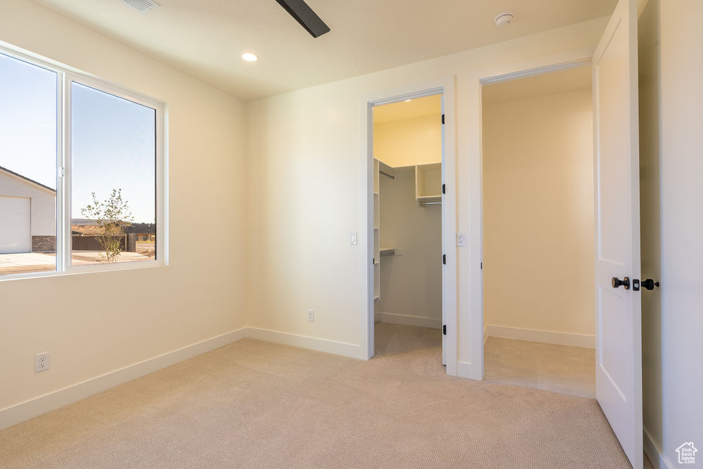 Unfurnished bedroom with light carpet, a spacious closet, ceiling fan, and multiple windows