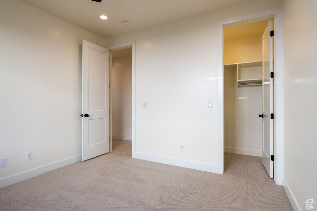 Unfurnished bedroom featuring a walk in closet, a closet, and light carpet