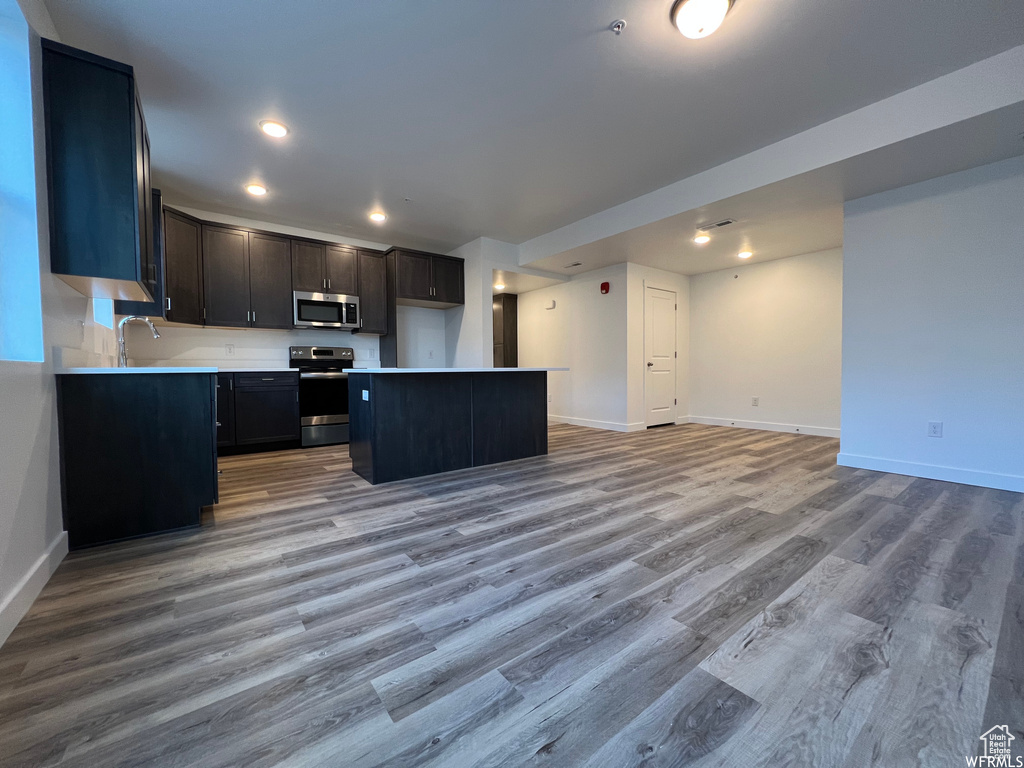 Kitchen with appliances with stainless steel finishes, a kitchen island, sink, and wood-type flooring