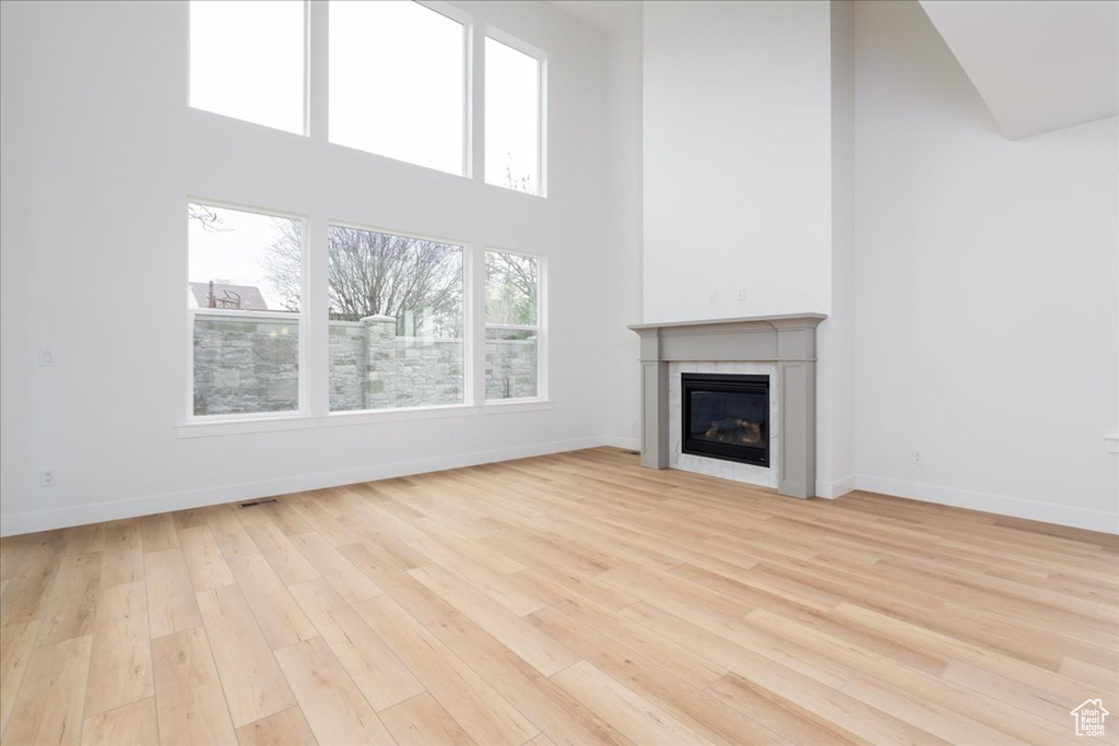 Unfurnished living room featuring a towering ceiling, light wood-type flooring, and a fireplace