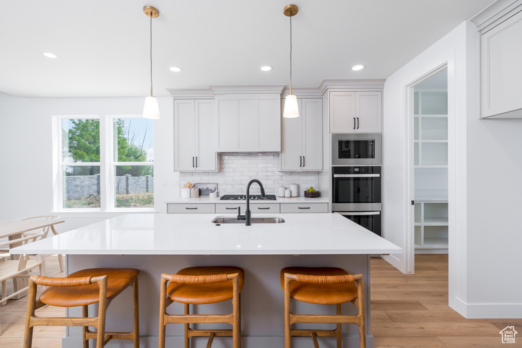 Kitchen featuring light hardwood / wood-style floors, backsplash, a center island with sink, hanging light fixtures, and stainless steel microwave