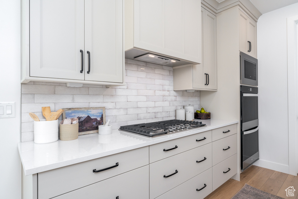 Kitchen featuring light hardwood / wood-style flooring, stainless steel appliances, tasteful backsplash, custom exhaust hood, and white cabinets