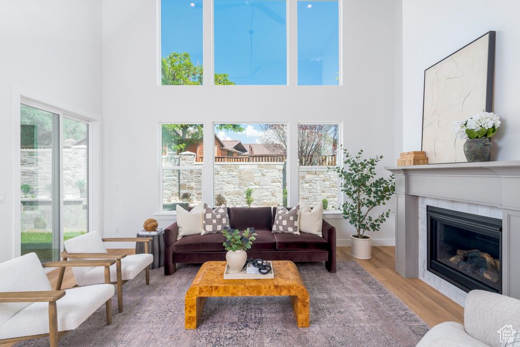 Living room featuring a high ceiling, a healthy amount of sunlight, a tile fireplace, and wood-type flooring