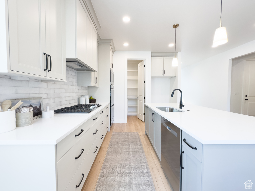 Kitchen featuring light hardwood / wood-style flooring, an island with sink, backsplash, sink, and appliances with stainless steel finishes