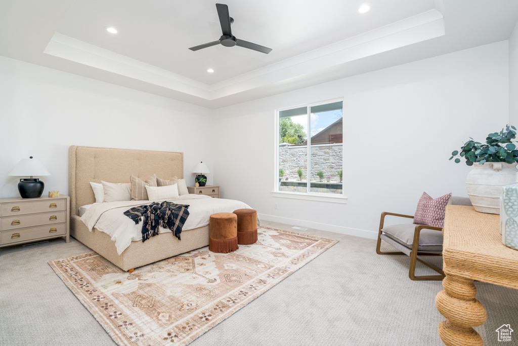 Bedroom with light colored carpet, ceiling fan, and a tray ceiling