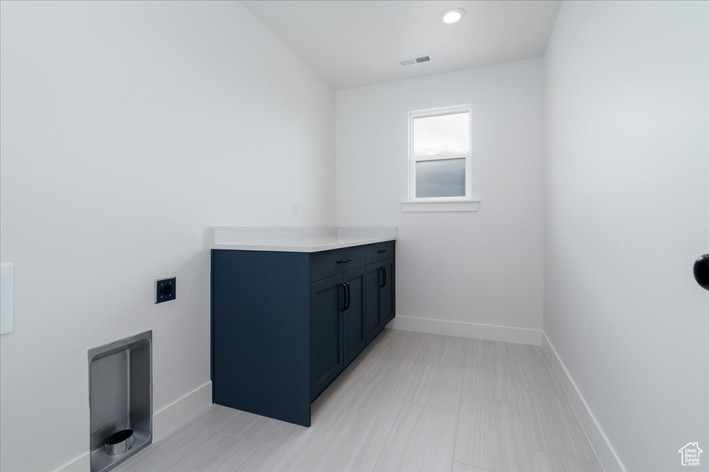 Laundry room with electric dryer hookup, light tile flooring, and cabinets