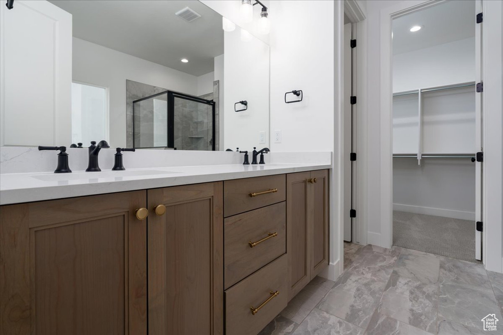 Bathroom with large vanity, a shower with door, dual sinks, and tile flooring