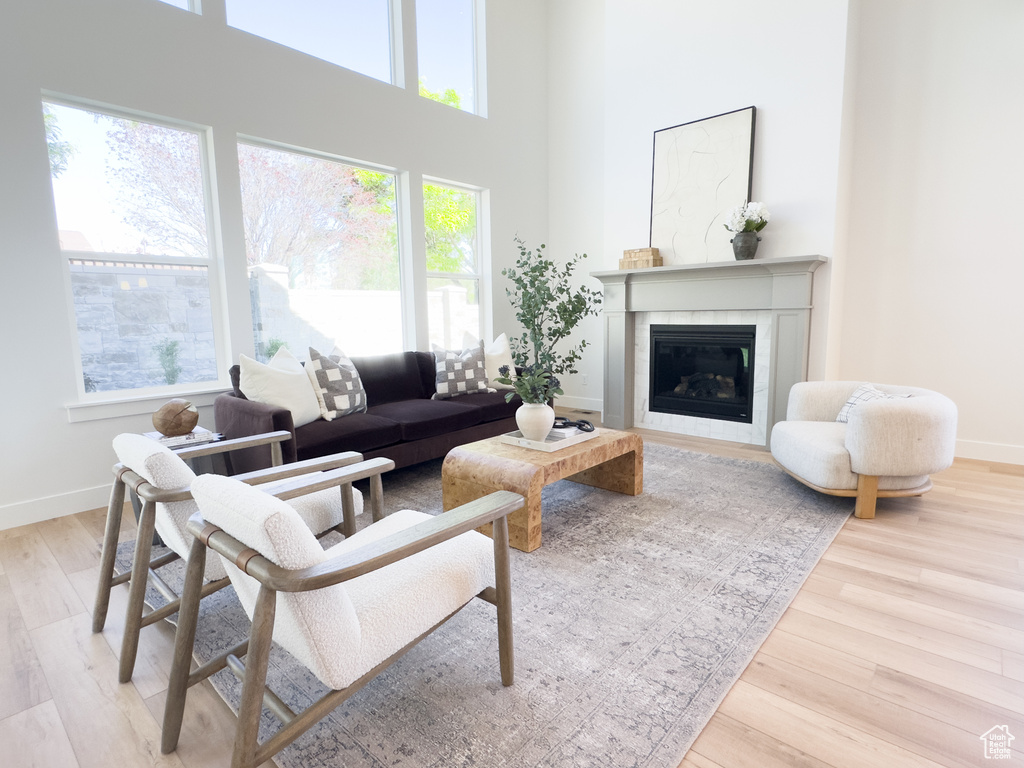 Living room featuring a towering ceiling, plenty of natural light, a tile fireplace, and light wood-type flooring