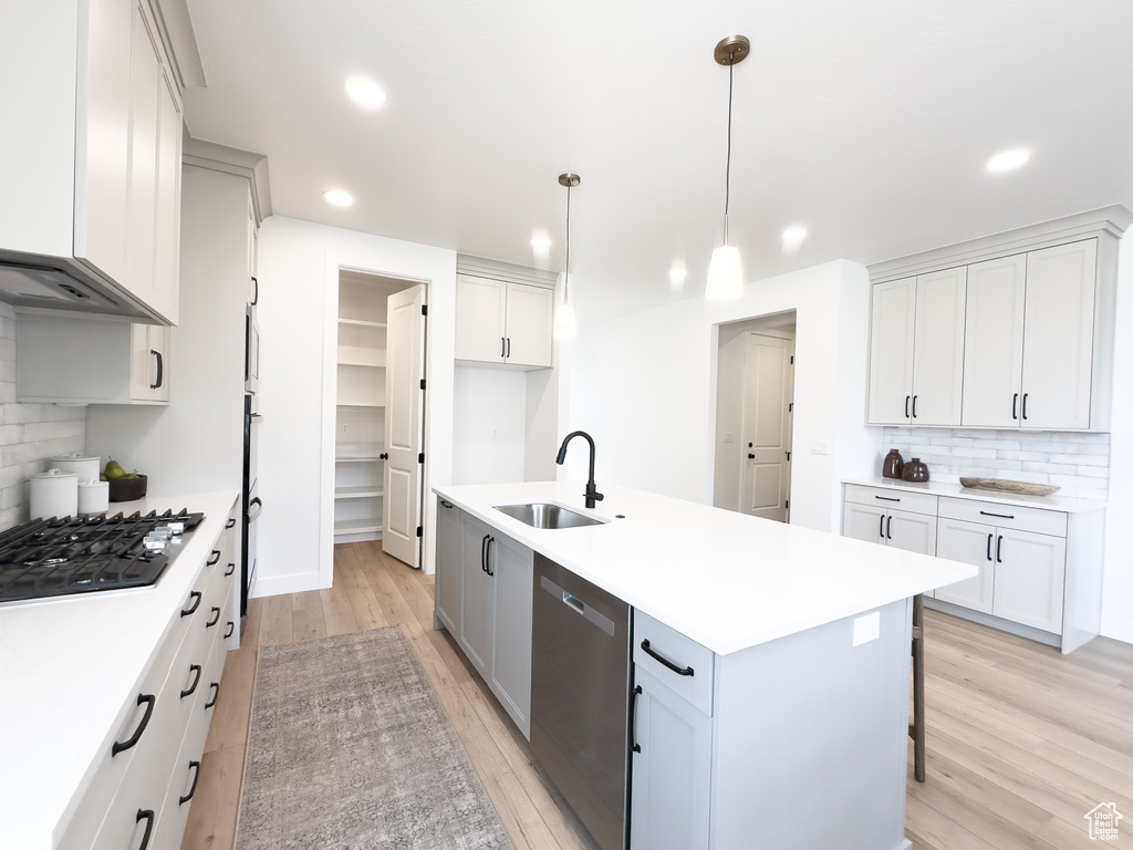 Kitchen featuring light hardwood / wood-style flooring, sink, tasteful backsplash, and a kitchen island with sink