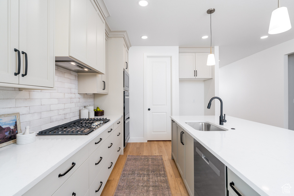 Kitchen with hanging light fixtures, light wood-type flooring, stainless steel appliances, sink, and tasteful backsplash