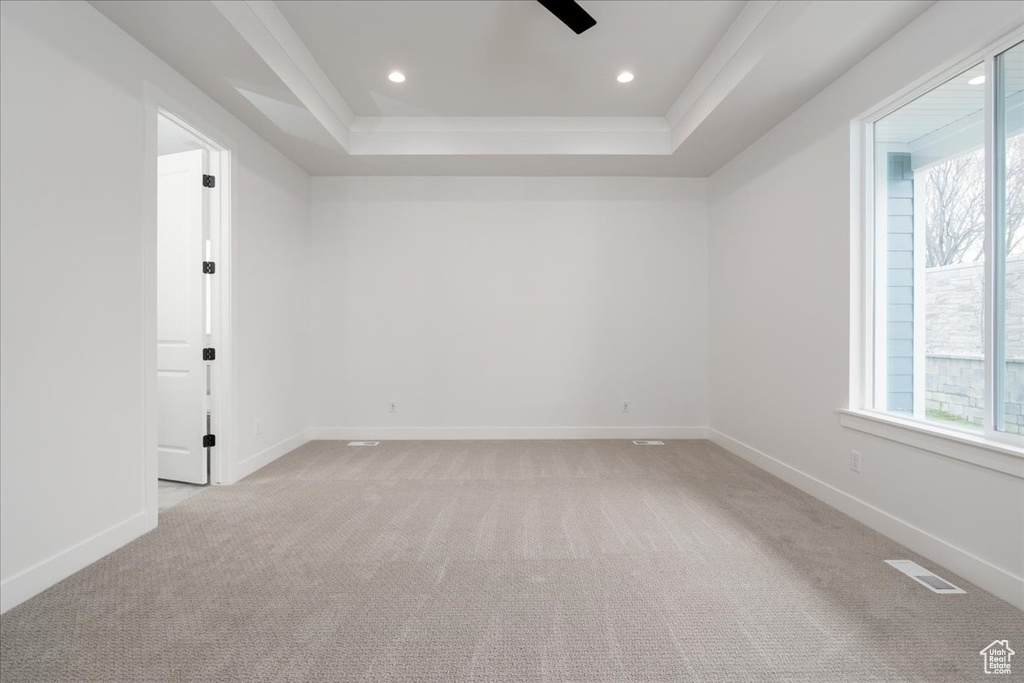 Unfurnished room featuring a tray ceiling, light colored carpet, and ceiling fan