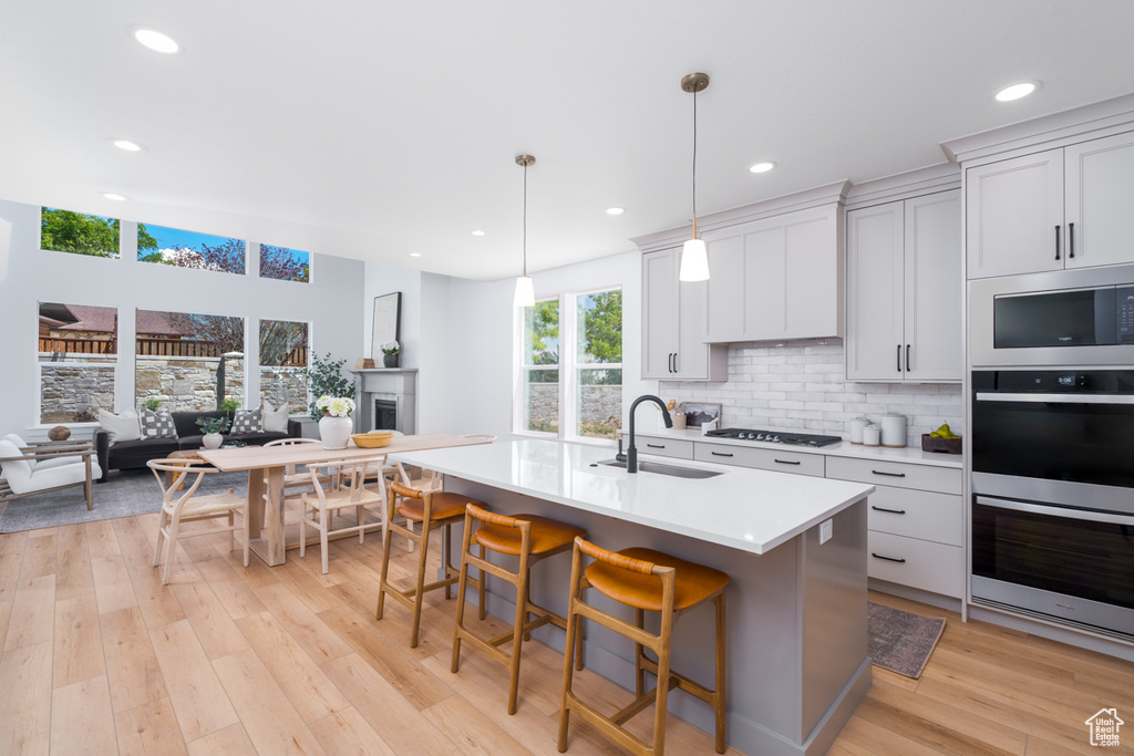 Kitchen with light hardwood / wood-style flooring, tasteful backsplash, black microwave, a kitchen bar, and double oven