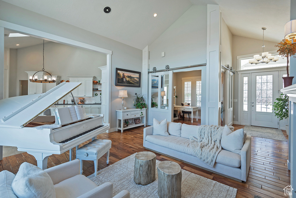 Living room featuring a barn door, high vaulted ceiling, a notable chandelier, and dark hardwood / wood-style flooring
