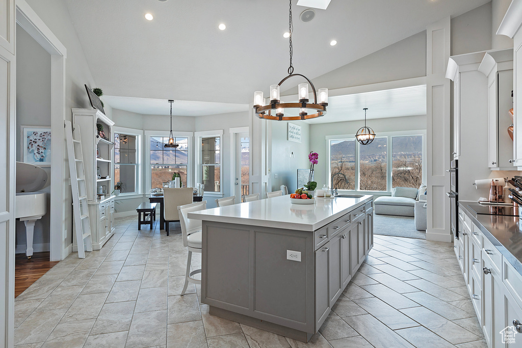 Kitchen with light tile floors, vaulted ceiling, an island with sink, and decorative light fixtures