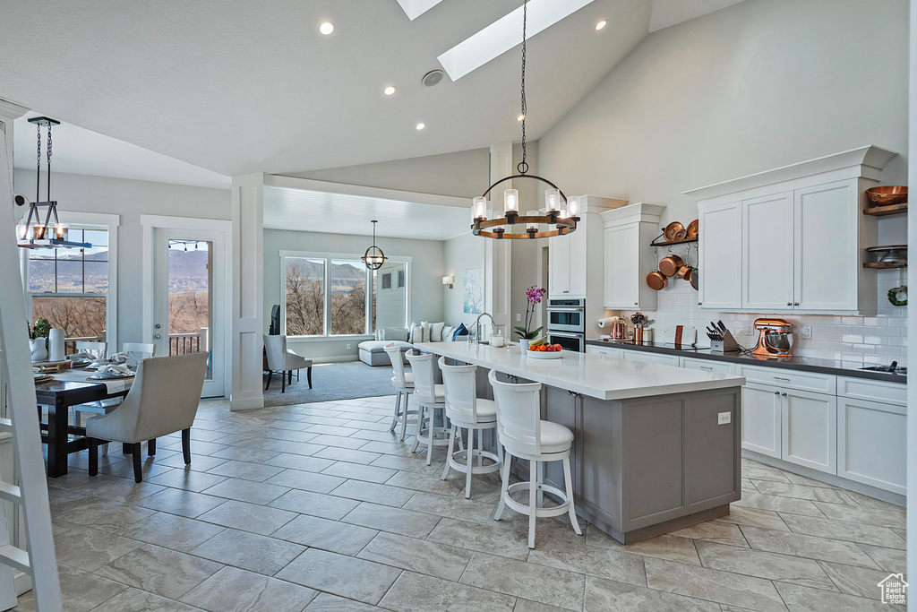Kitchen with white cabinets, high vaulted ceiling, a skylight, hanging light fixtures, and a kitchen island with sink