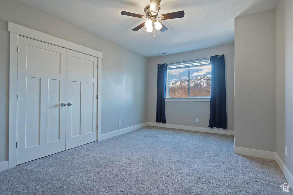 Unfurnished bedroom with a textured ceiling, a closet, light carpet, and ceiling fan